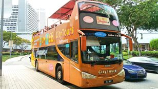 Vibrant FunVee bus, tourists aboard, traverses Singapore's streets, an exciting journey painted in bright orange and enthusiasm.